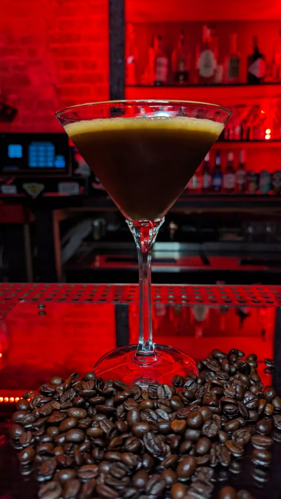 A martini sits on the bar with coffee beans in the background.