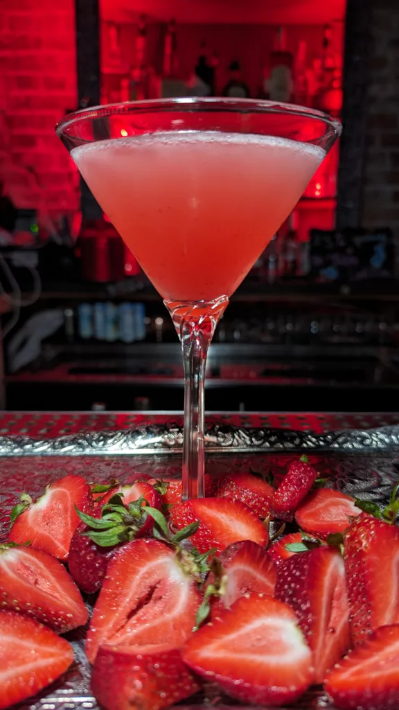 A strawberry martini sitting on a bar, surrounded by strawberries.