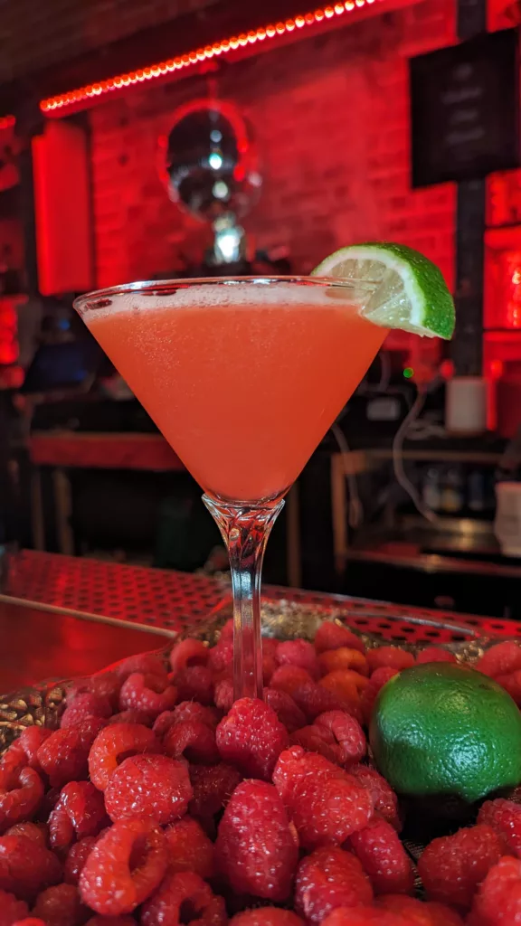 A cocktail with raspberries at a bar.