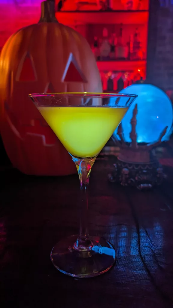 A cocktail with a yellow liquid in front of a pumpkin at the bar.